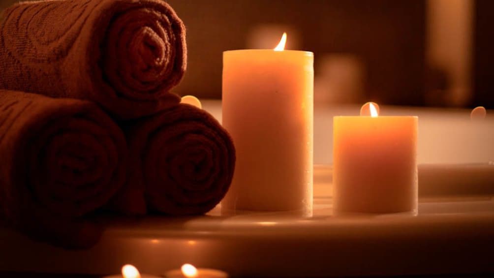 Close up of towels and lit candles by bathtub.