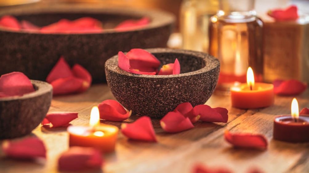 Close up of red rose pedals and lit candles.