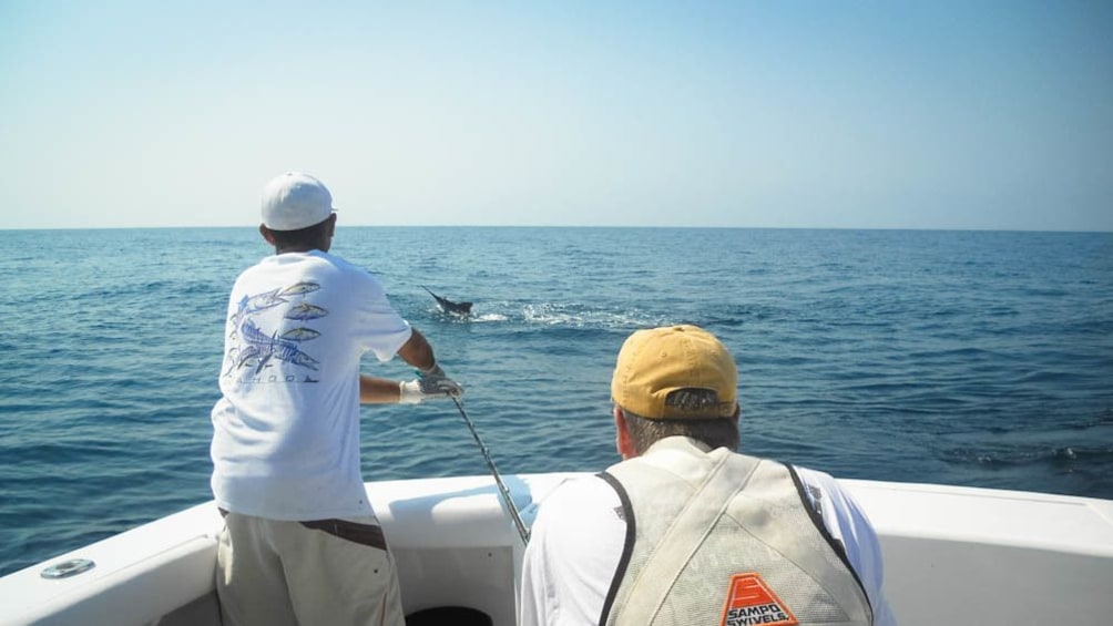 Two men in boat catching fish in ocean.