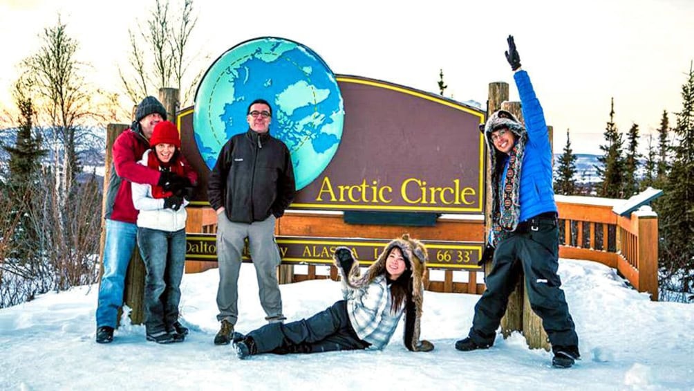 Several tourists shown posing in front of Arctic Circle sign.