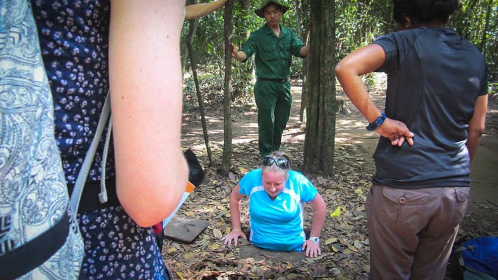 Woman entering Cu Chi tunnel while group members observe.