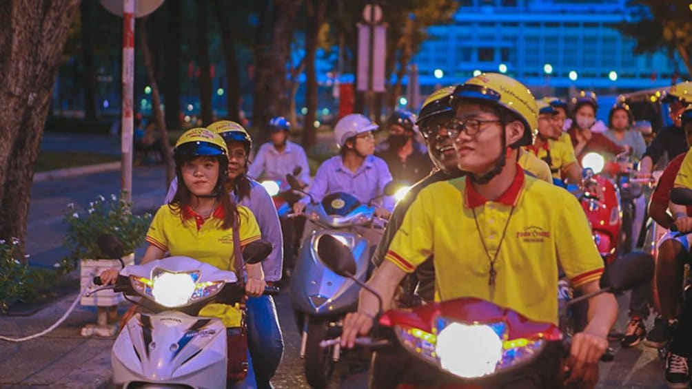 Tour group riding mopeds through the city at night.