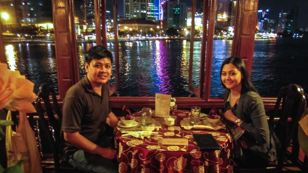 Couple having dinner by the waterfront at night, with few of city.