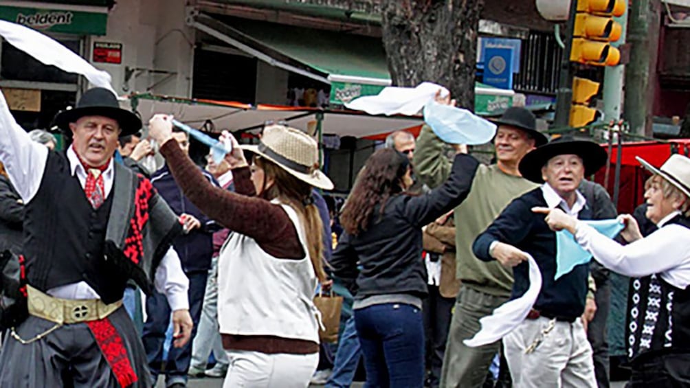 A group of men and women dancing in the street in traditional clothes and hats