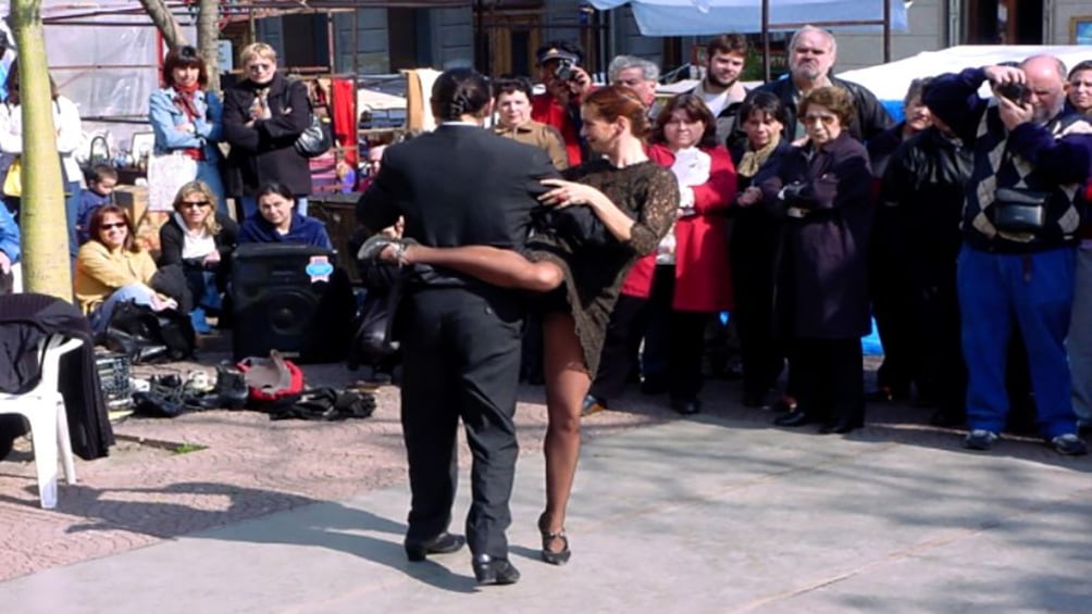 Group on the street surrounds two people dancing the Tango