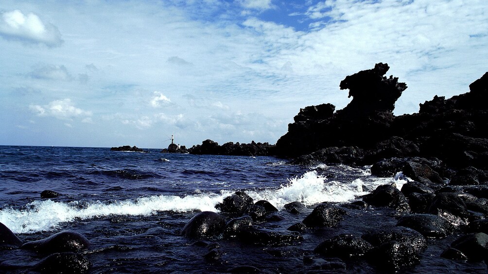 Man fishes in the distance of the rocky shore of Jeju Island