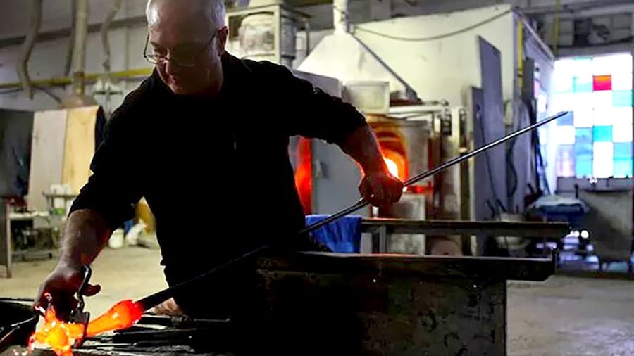Glass blower sculpts molten glass in his shop