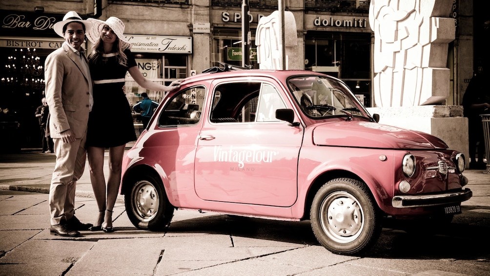 well dressed couple poses next to a red Fiat vehicle in Italy