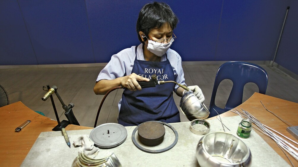 Person taking a blowtorch to a metal bowl in Royal Selangor