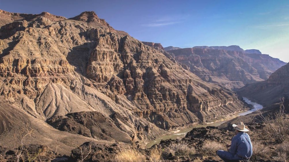 Landscape view of large canyon with man observing while sitting.