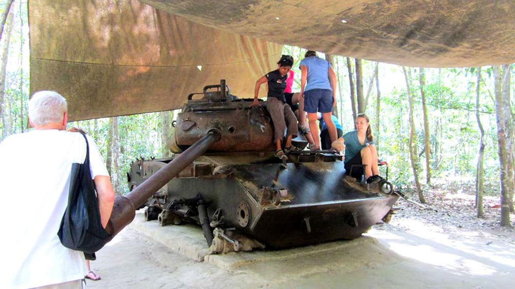 Tourists climb on a tank under a canopy during Tour of Cu Chi Tunnels