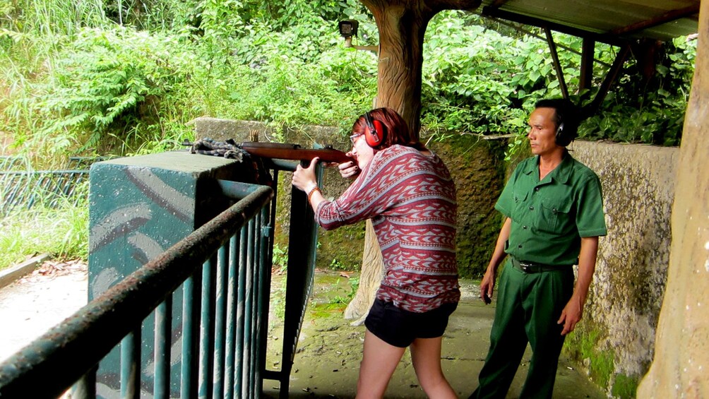 Woman shoots target practice with a guide clad in an olive green jumpsuit