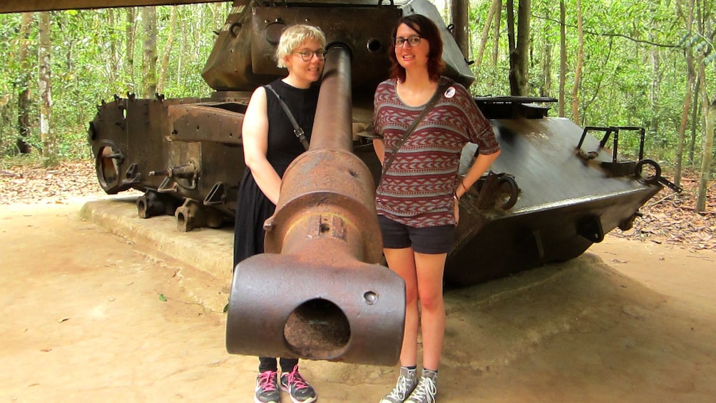 Two women pose with a tank as the barrel is pointed to the camera