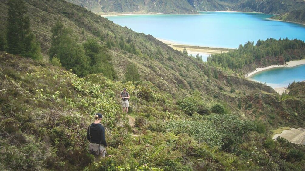 Group of people hiking down grassy hill surrounded by blue water.