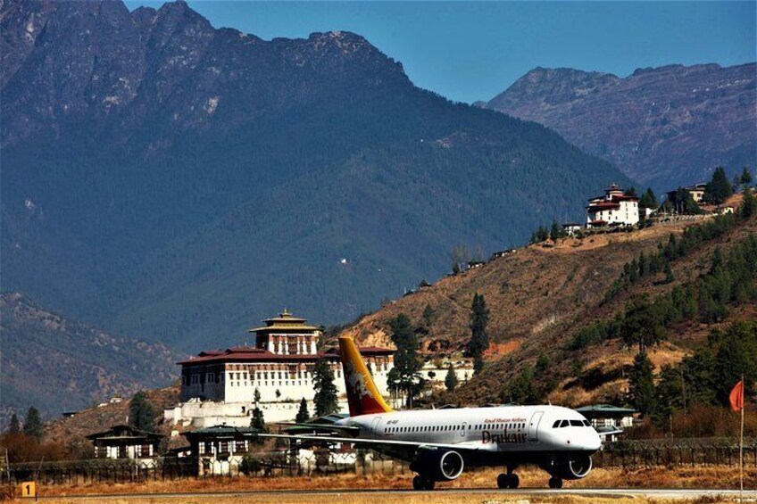 Paro International Airport- surrounded by mountains and Paro Fortress at the background.

