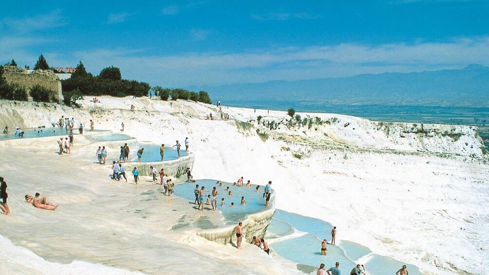 Landscape view of Pamukkale during the day with several people swimming.