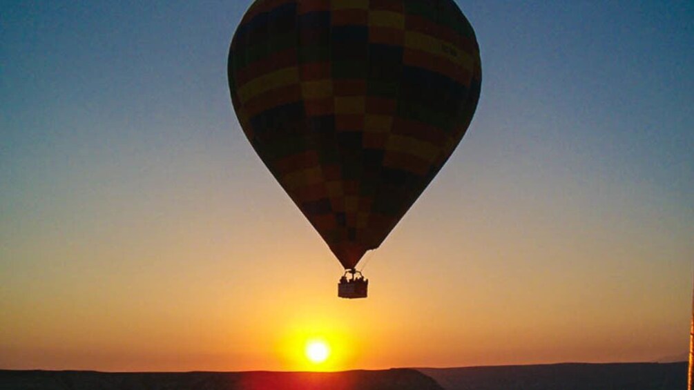 Hot air balloon silhouette floating over city at sunset.