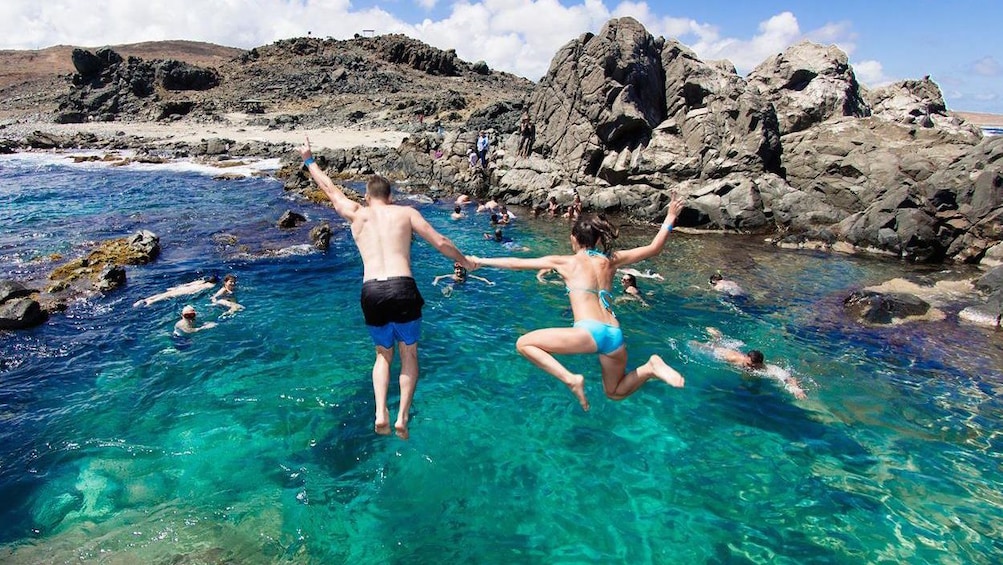 A couple jumps off a cliff into the ocean in Aruba