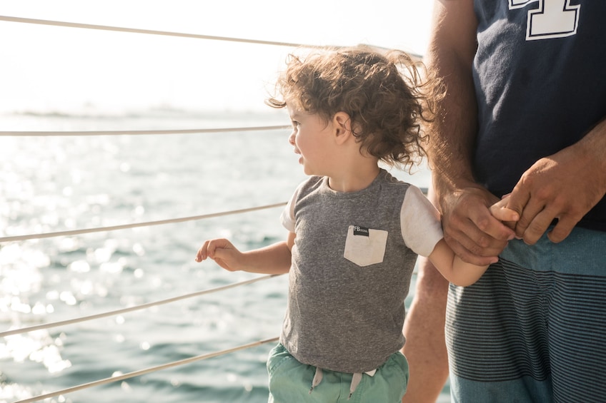 Show item 3 of 7. Young boy holds father's hand on catamaran off of Maui