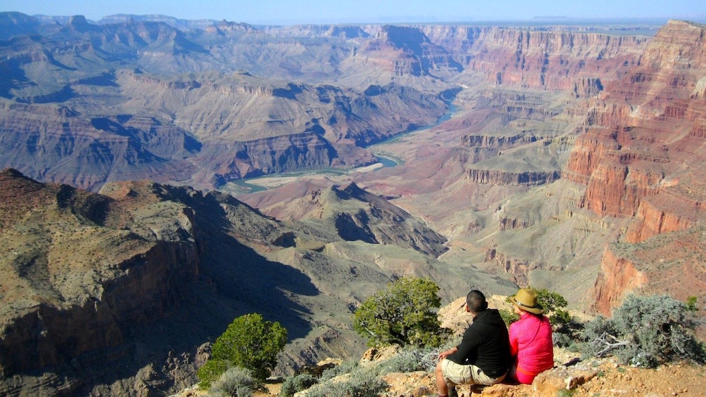 Two people sit and look at the Grand Canyon