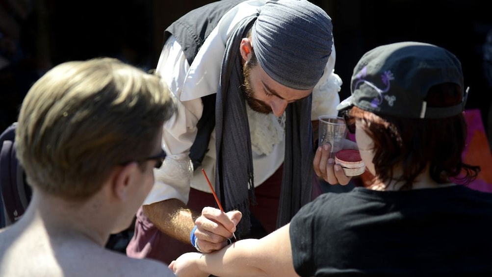 A pirate paints a temporary tattoo on a persons arm