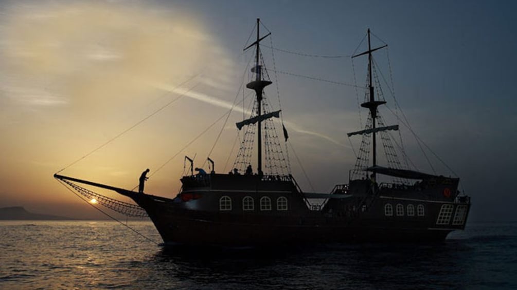 A silhouetted Pirate ship on the Greek coastline at dusk.