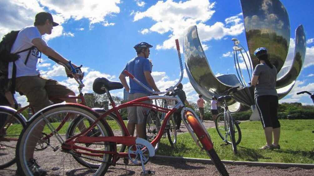 Cyclists stopped, observing local sculpture.