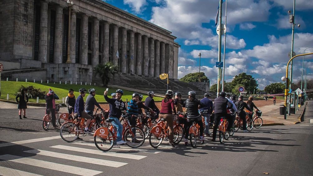 Several tourists on bikes in front of historical building.