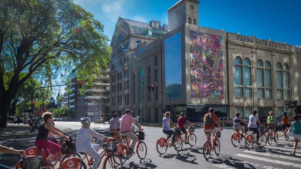 Several tourists on bikes riding near local building.