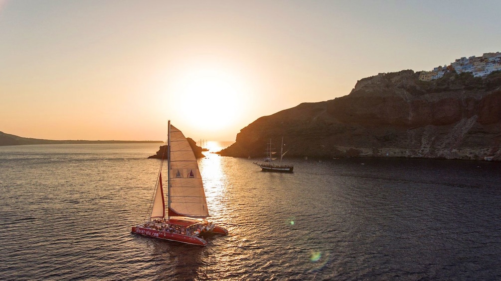 Catamaran sailing while sun sets in Santorini