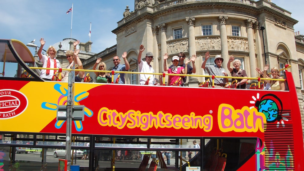 People waving from the top of a Hop-On Hop-Off bus in Bath