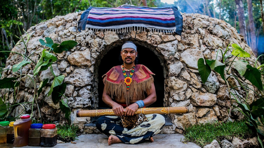 Shaman sitting in front of a rock hut in Cancun
