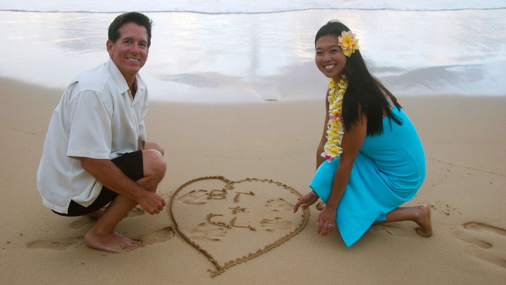 Couple drawing heart in sand in Kauai