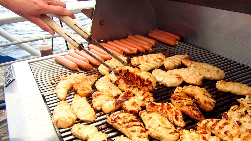 Show item 3 of 8. Chef cooking chicken and hotdogs on the grill on the Molokini Wild Side Eco Adventure in Maui