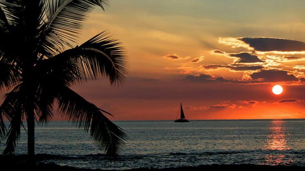 View from beach of sunset with sailboat around Big Island