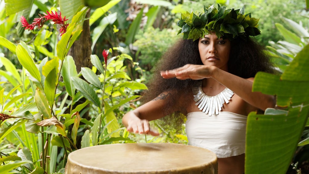Woman in traditional clothing plays drum in Kauai