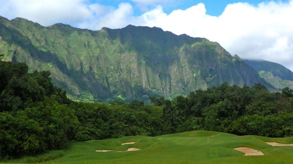 Show item 1 of 5. Dramatic cliffs rise behind a golf green at Ko'olau Golf Club