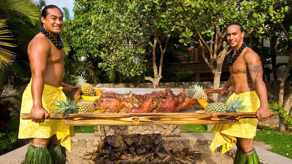 Two males in performance outfits with a roasted pig for the Te Au Moana Luau in Maui 