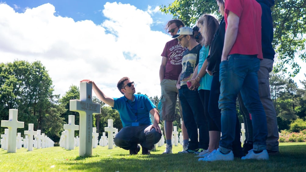 Guide touching cross gravestone as group listens 