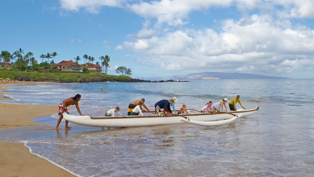 Small group pushing canoe towards the water in maui