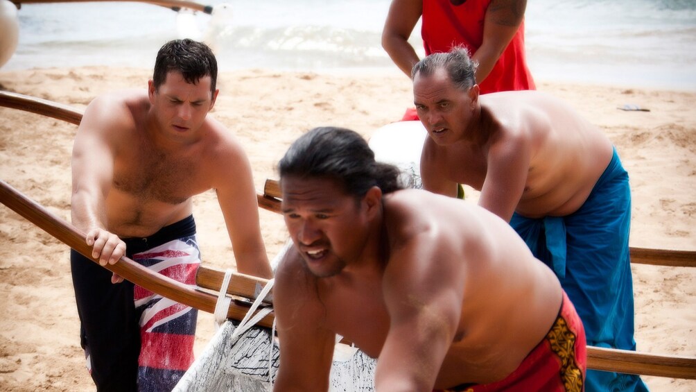 Four men pull outrigger canoe up on the beach
