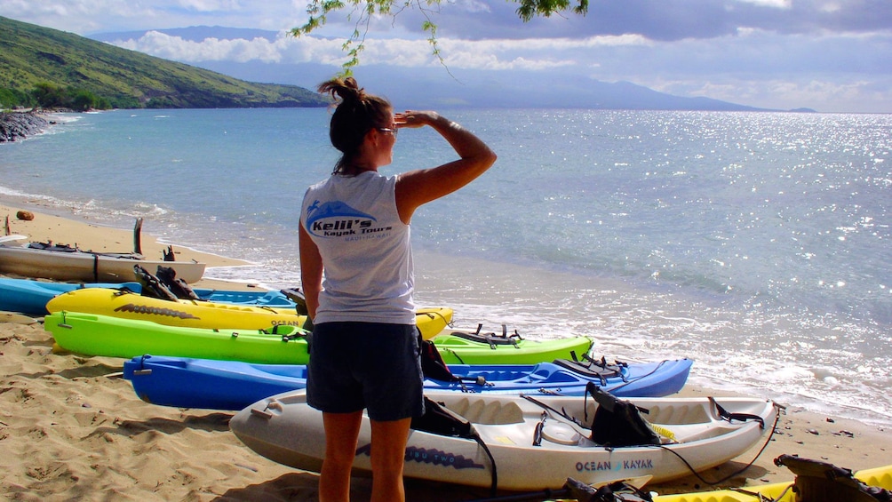 Woman looking out at ocean with kayaks beached on sand in Maui 