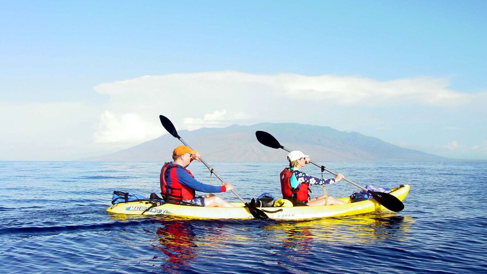 People in tandem kayak paddle through smooth water off of Maui