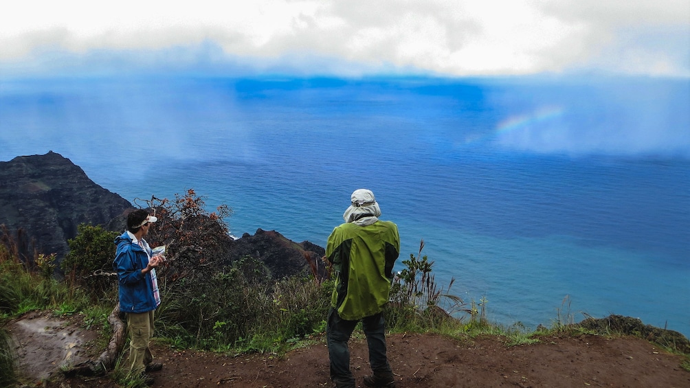 Hikers shown from behind at mountain peak observing beautiful view of ocean.