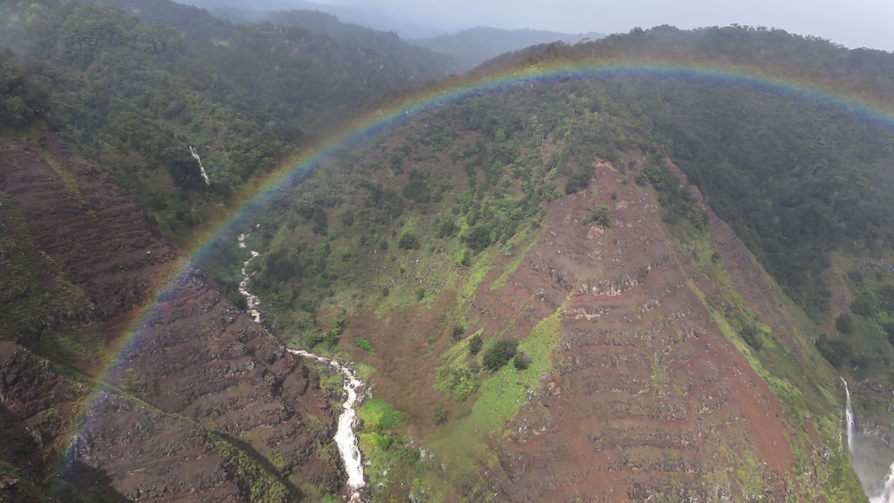 Aerial view of grassy mountains with rainbow arching across.