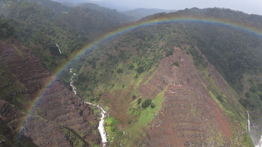 Aerial view of grassy mountains with rainbow arching across.