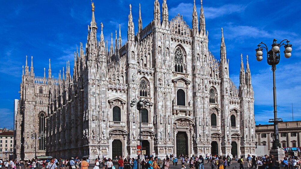 Angled exterior view of Milan Cathedral with hundreds of people walking about.