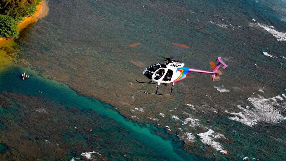 helicopter flying over ocean by island shore in Kauai
