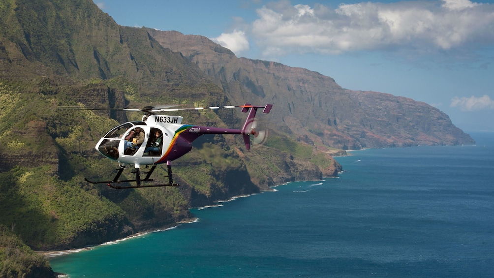helicopter flying over ocean by island cliffs in Kauai