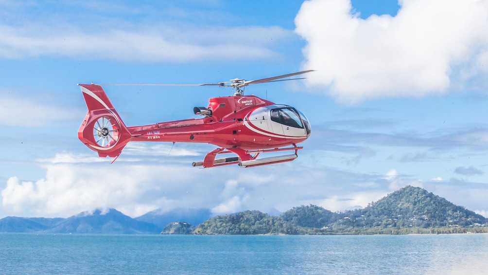 Red tour helicopter shown flying over ocean waters.